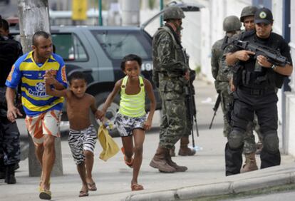 Una familia brasileña pasa ante policías y soldados en el Complexo Alemão, donde tiene lugar una gran operación contra los <i>narcos.</i>