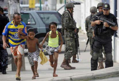 Una familia brasileña pasa ante policías y soldados en el Complexo Alemão, donde tiene lugar una gran operación contra los <i>narcos.</i>