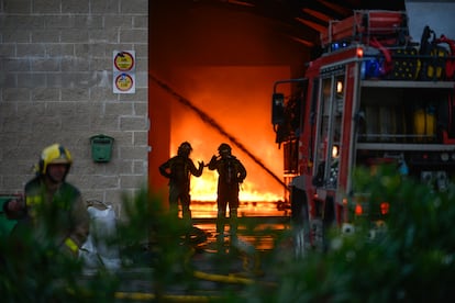 Dos bomberos examinan la nave mientras se intenta extinguir el incendio en Sarria de Ter.