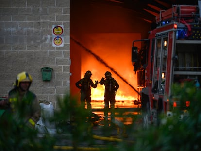 Dos bomberos examinan la nave mientras se intenta extinguir el incendio en Sarria de Ter.