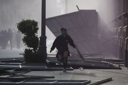 Una mujer corre entre los muros de contención derribados en las puertas del Palacio Nacional de Ciudad de México.