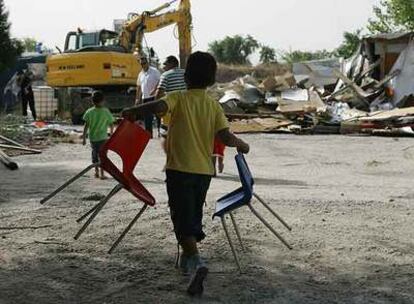 Un niño transporta dos sillas mientras una excavadora derriba una chabola en el poblado de El Salobral.