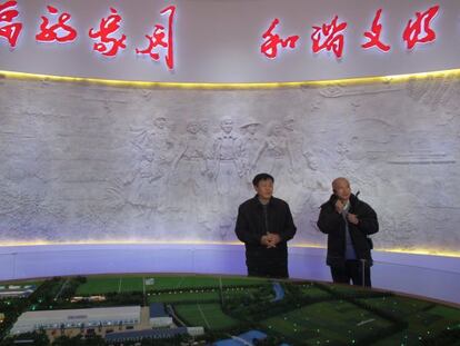 Chang Desheng, secretario general del PCCh en el pueblo, en el museo local ante un mural donde está retratado.