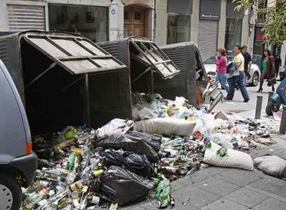 Un grupo de viandantes pasa junto a unos contenedores de vidrio volcados en Chueca.