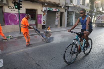 Un ciclista pasa por la calzada de una calle de Elche mientras los operarios eliminan las señales del carril bici.