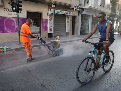 Un ciclista pasa por la calzada de una calle de Elche mientras los operarios eliminan las señales del carril bici.