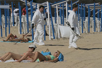 Varias personas toman el sol en la playa de La Concha, en presencia de operarios de limpieza del chapapote.