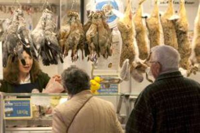 Dos personas compran en una pollería que ofrece piezas de caza menor en el Mercado de Vitoria. EFE/Archivo