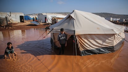 Dos niños sirios son fotografiados junto a su casa, una tienda de campaña, ahora inundada debido a las inundaciones a causa de las fuertes lluvias que cayeron sobre el campo de refugiados de Ma'arrat al-Nu'man, en Siria, el 17 de diciembre de 2020.