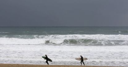Unos surfistas caminan por la playa de La Zurriola de San Sebastián donde se registra un fuerte temporal de viento y lluvia.