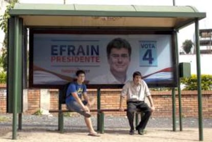 Fotografía del domingo 7 de abril de 2013 de dos hombres esperando el autobús junto a un cartel con propaganda del candidato presidencial paraguayo del gobernante Partido Liberal Radical Auténtico (PLRA), Efraín Alegre, en Asunción. EFE/Archivo