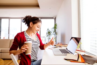 Smiling woman with coffee to go at desk at home