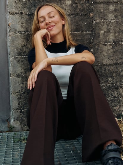 Ester Expósito lleva top de punto con cuello halter blanco, top de manga corta con cuello alto, pantalón de pinzas y zapatillas con hebilla dorada, todo de MIU MIU.