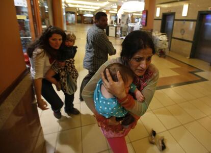 Dos mujeres son protegidas por policías armados para salir del interior del centro comercial.