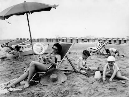 Una mujer lee en la playa bajo una sombrilla, en 1962.