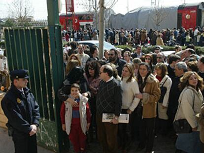 Una gran fila de personas se dirigen a votar en el barrio de El Pozo; al fondo, el tren en el que viajaban las víctimas del atentado.