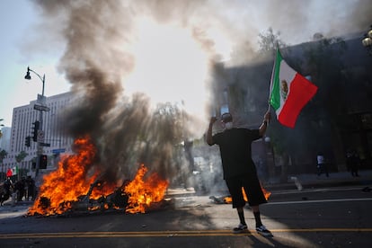 Un taxi Waymo incendiado por manifestantes arde cerca del centro de detención metropolitano del centro de Los Ángeles, este domingo, tras la protesta por la redada de inmigración de anoche.