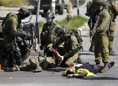 El soldado acuchillado y el palestino que se haba disfrazado de reportero para poder atacarlo yacen en el suelo rodeado de un grupo de soldados israeles.