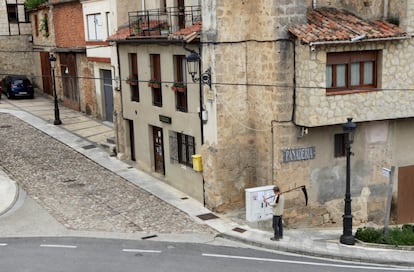 Un hombre con guadaña pasa por delante de una panadería en Frías (Burgos).