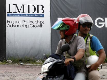 Dos hombres pasan en moto frente a un cartel del fondo soberano 1MDB, en febrero de 2016 en Kuala Lumpur (Malasia).
