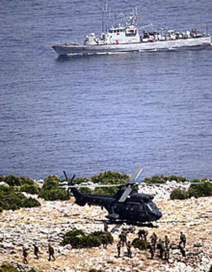 Soldados españoles descargan material de un helicóptero en la isla Perejil, mientras una fragata escolta y protege la operación.