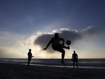 Homens jogam futebol na praia de Copacabana.