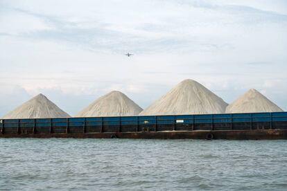 Montañas de material para la construcción, probablemente con arena mezclada con granito, entran en un puerto occidental de Singapur en barco.