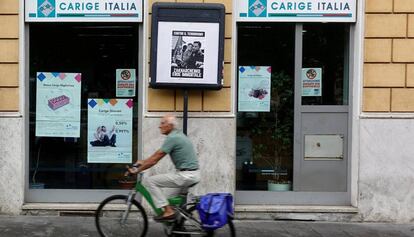 Un hombre pedalea en una bicicleta junto a una sucursal de la Banca Carige en Roma
