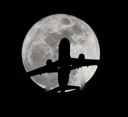 Un avión de pasajeros en ruta hacia el aeropuerto internacional de Los Ángeles pasa por delante de una luna llena sobre Whittier (California).