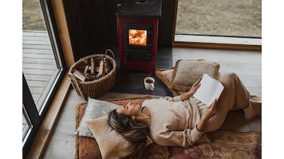 Una chica leyendo un libro enfrente de su chimenea.