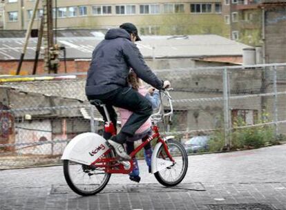 Un hombre con un niña sentada en la barra de una bicicleta del <b>Bicing</b> en Barcelona.