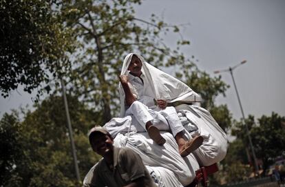 Un hombre indio vuelve de la lavandería subido en una pila de ropa en un 'rickshaw', en Delhi, India. 11 de junio de 2014.