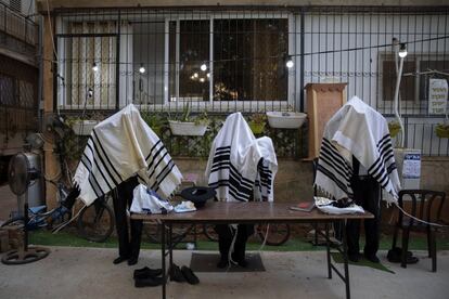 Judíos ultra ortodoxos rezan cubiertos con mantos de oración, en el patio de su casa, en Bnei Brak (Israel). La última cifra de nuevos positivos diarios en el país bajó hoy de la barrera de los mil, lo que confirma la mejoría de la situación de la pandemia tras un mes de confinamiento y el inicio de una lenta desescalada.