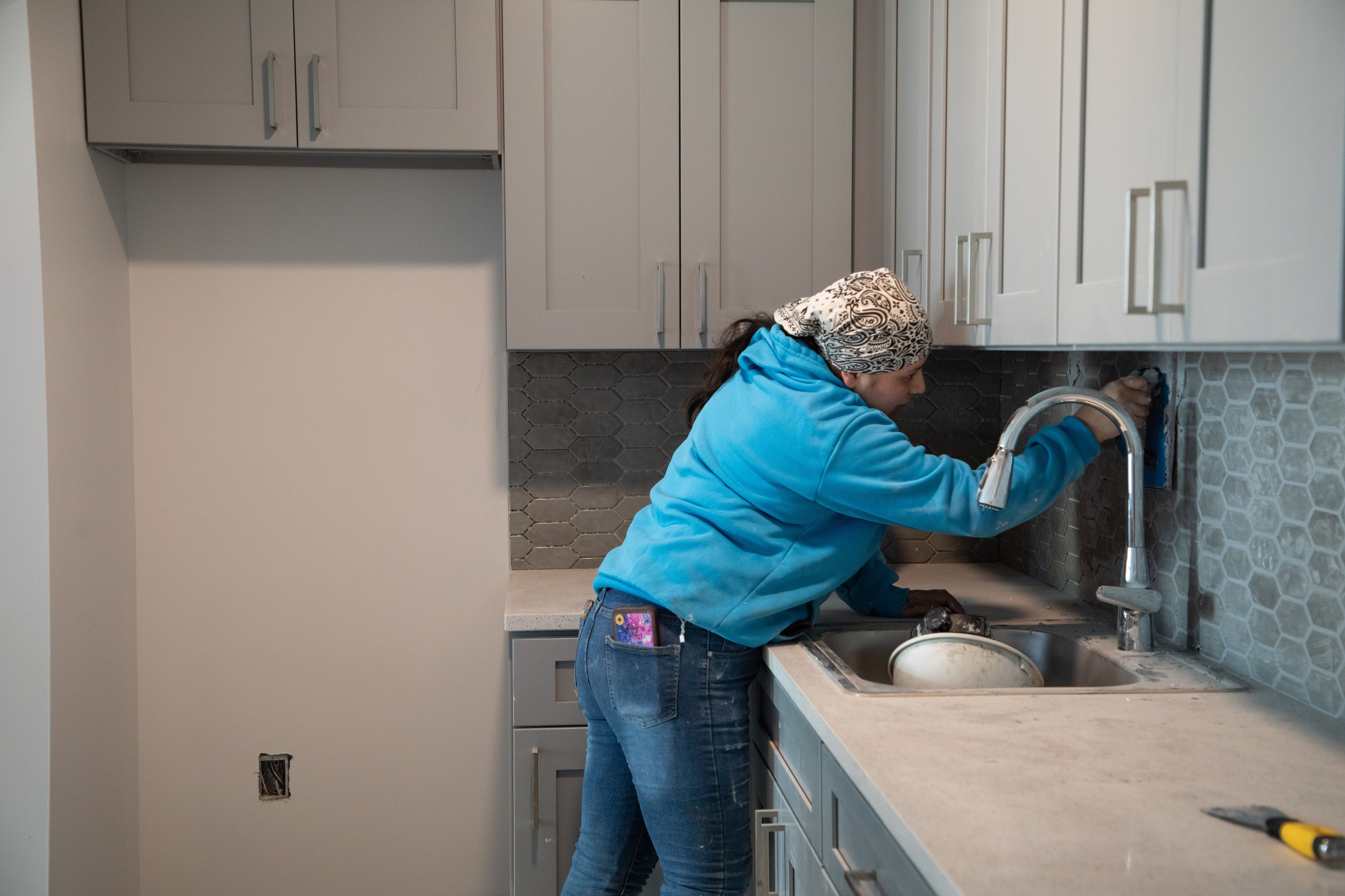 Brenda distribuye mezcla en las juntas de los baldosines de la cocina de una construcción en Brooklyn. 