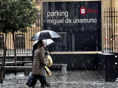 Dos personas se protegen de la intensa granizada caída hoy en Bilbao mientras el Gobierno Vasco mantiene activa la alerta naranja por fuertes rachas de viento y oleaje costero, el 27 de diciembre.