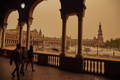 Varias personas pasean por la Plaza de España durante la tarde de lluvia en Sevilla con nube de polvo, este jueves.