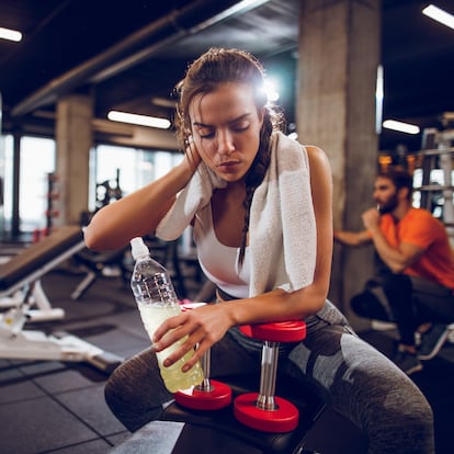 Fitness woman drinking water while sitting and resting at the gym