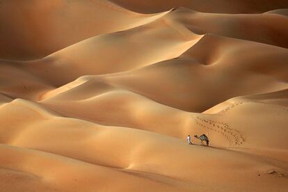 Un hombre emiratí camina con su camello a través del desierto de Hameem, a unos 170 kilómetros al oeste del Emirato del Golfo de Abu Dhabi.