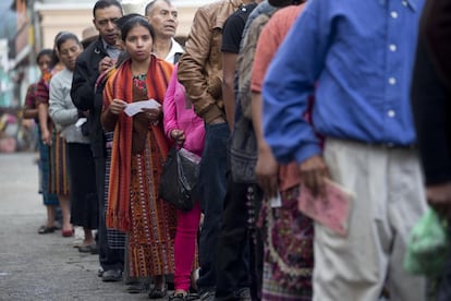 Un grupo de personas esperan en fila para poder votar en colegio electoral en San Juan Sacatepéquez.