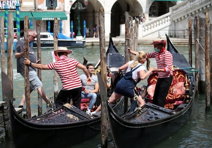 Gondoleros ayudan a varios turistas a subir a sus embarcaciones en un canal de Venecia.