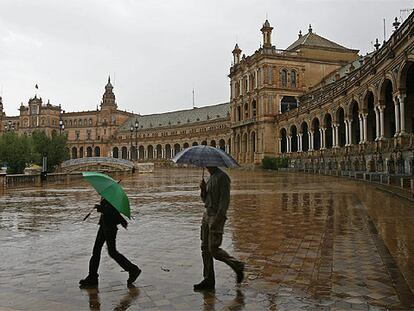 Dos turistas pasean con sus paraguas por la Plaza de España de Sevilla.