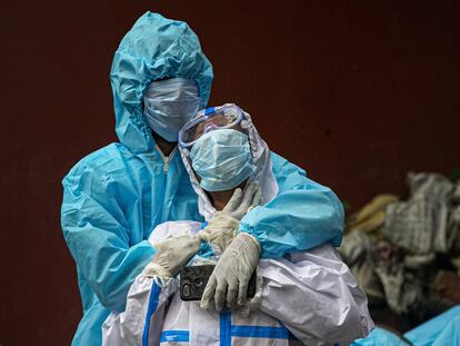 Dos mujeres indias con protección velan el cuerpo de un familiar fallecido por la covid, en un crematorio de Gauhati (India).)