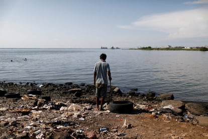 Un hombre se encuentra junto a una pila de basura en las orillas del lago de Maracaibo. Los desperfectos acumulados en calles y carreteras se han convertido en un problema.