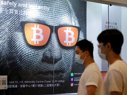 Dos personas pasan frente a un anuncio de Bitcoin en Hong Kong.