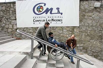 Dos personas ayudan a un minusválido a bajar las escaleras en el recinto ferial de la Casa de Campo.