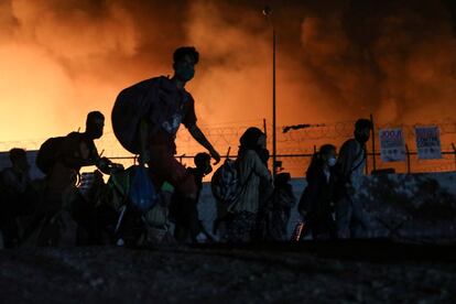 Tras la reunión del primer ministro griego, Kyriakos Mitsotakis, con varios de sus ministros se ha anunciado la declaración del estado de emergencia en Lesbos y se han enviado refuerzos policiales. En la imagen, migrantes cargan con sus pertenencias mientras huyen del incendio.