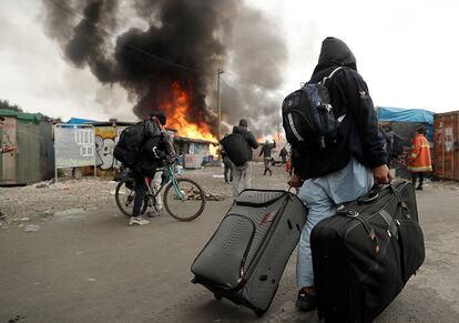 Un migrante empuja sus maletas durante el incendio del campamento de Calais durante la jornada de evacuación.