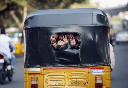 Niños indios saludan desde la ventana trasera de un auto rickshaw en Hyderabad, India. Rickshaws se les llama popularmente a un medio barato de transporte.