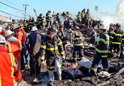 Docenas de bomberos de Nueva York trabajan entre los restos del avión de American Airlines que se estrelló ayer en el barrio de Queens.
