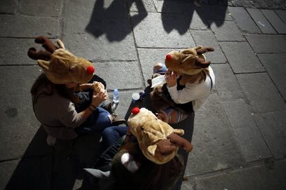 Unas niñas meriendan con unos gorros navideños sentadas sobre el mármol.